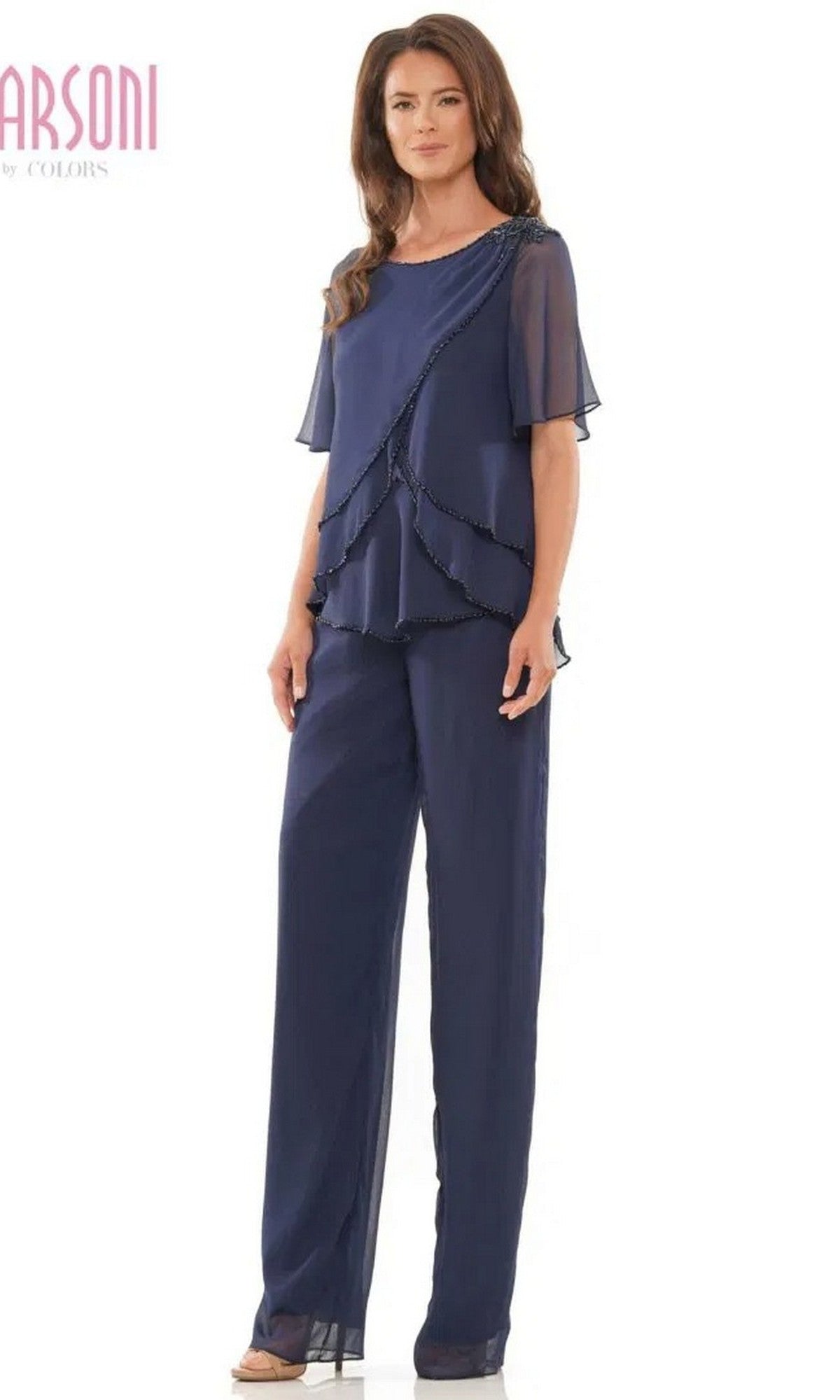 A woman wears the Marsoni M321, a long formal pantsuit in navy blue chiffon featuring sheer short sleeves and layered ruffle detailing on the top.